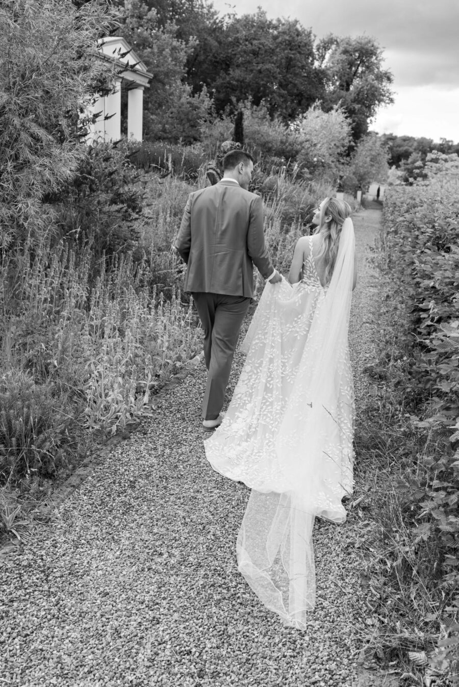 Brautpaar spaziert durch Gartenweg im Sommer.