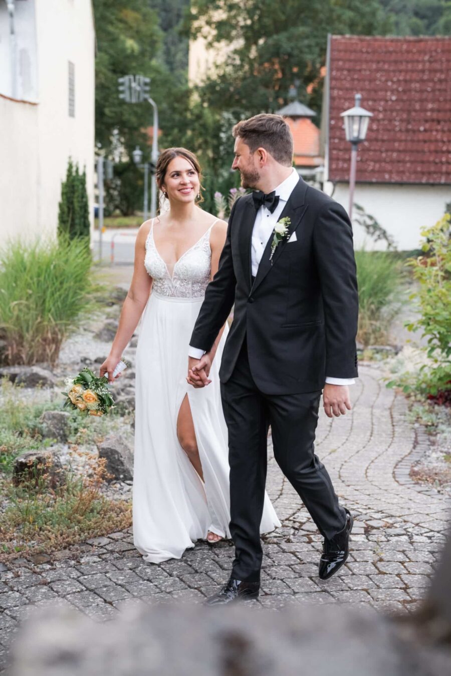 Brautpaar spaziert Hand in Hand im Gartenweg