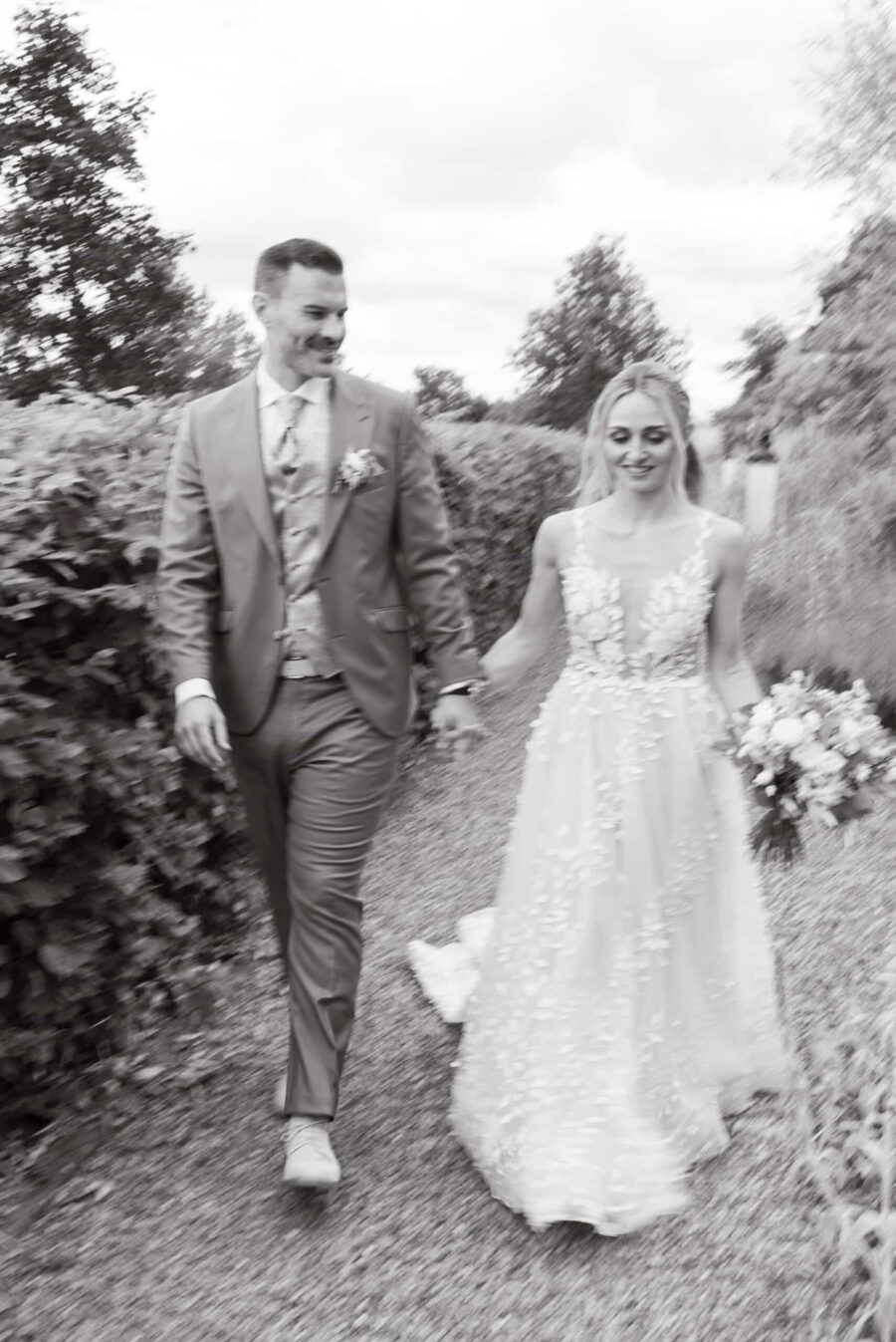 Brautpaar spaziert im Garten mit Blumenstrauß