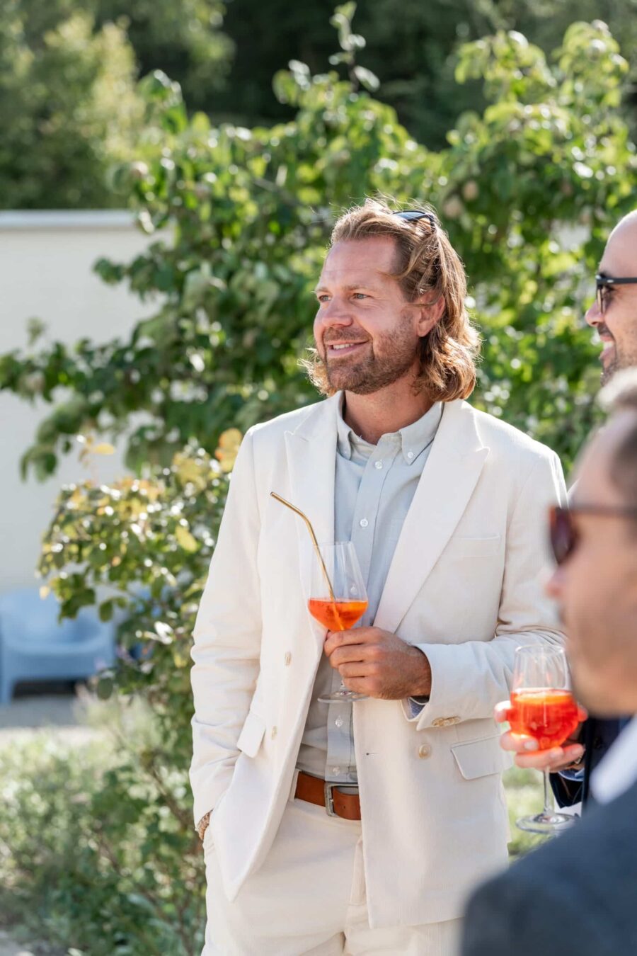 Hochzeit Villa Oriental | Editorial Summer Vibes & Live Cooking 441 Gast in Sommeranzug mit Aperitif im Garten.