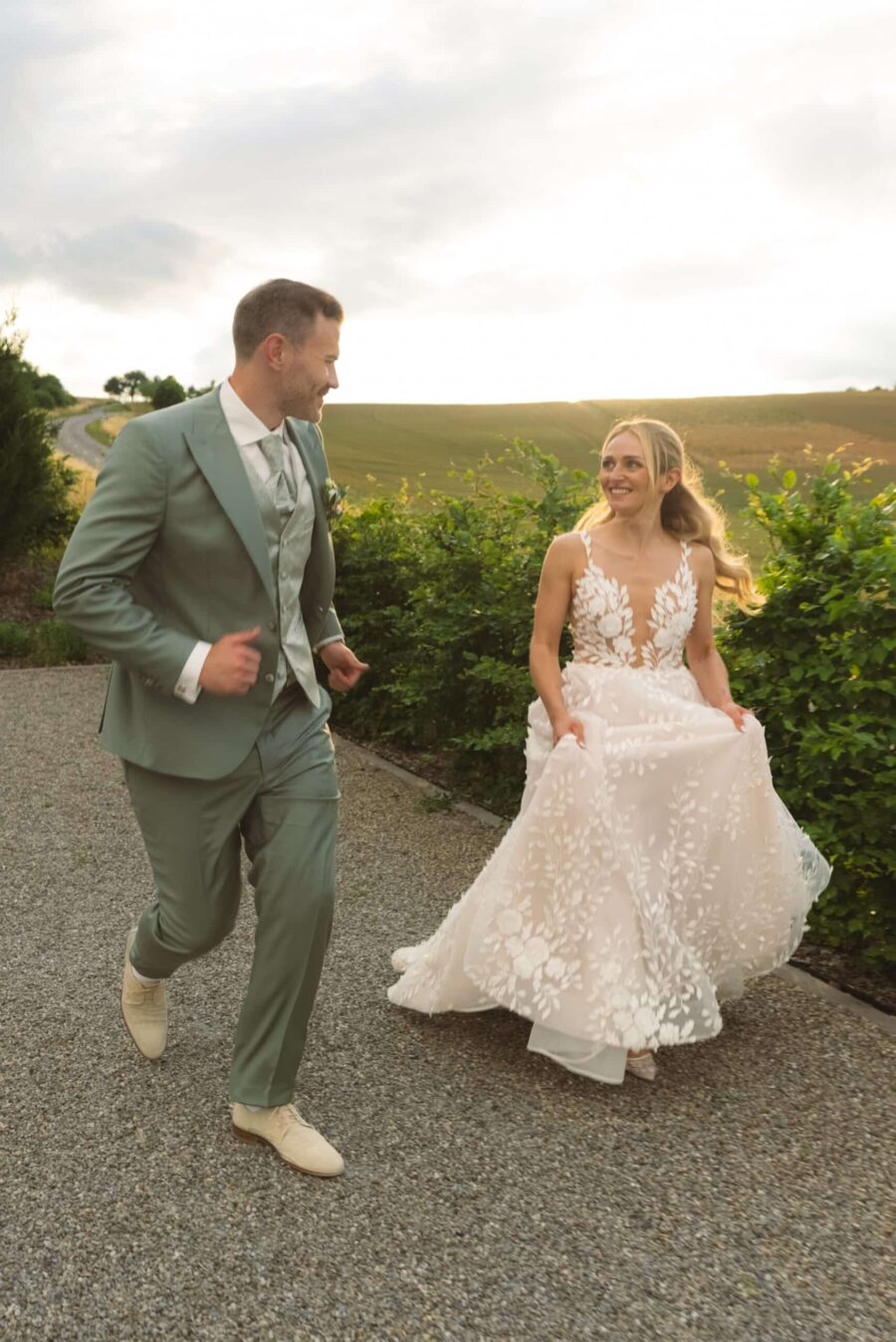 Brautpaar läuft fröhlich auf Gartenweg im Sonnenuntergang