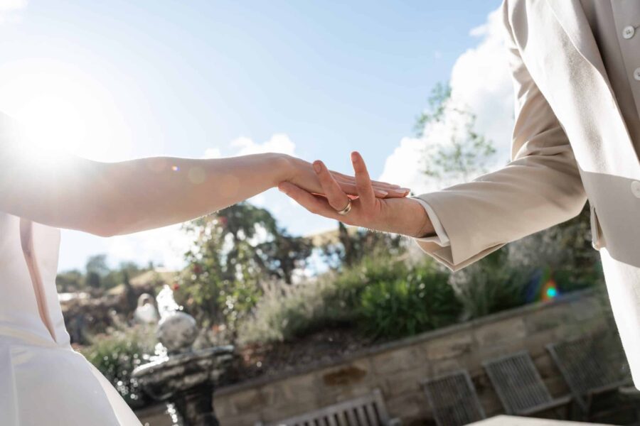Hände des Brautpaars im Sonnenschein im Garten