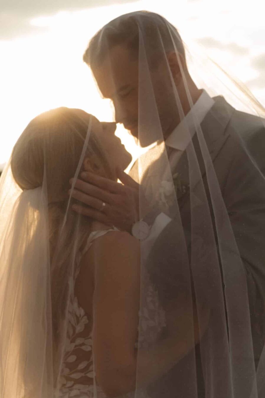 Brautpaar küsst sich unter dem Schleier im Sonnenlicht