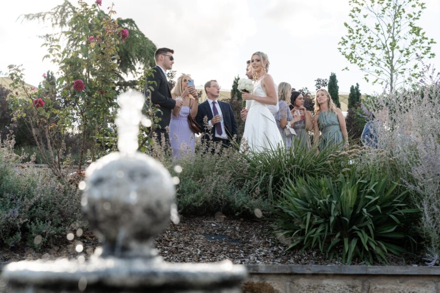 Hochzeitsgesellschaft im Garten mit Braut und Blumen.