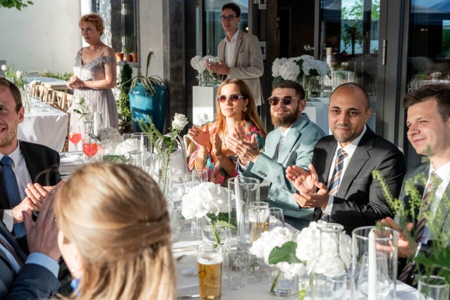 Gäste applaudieren bei Hochzeitstafel im Sommergarten.