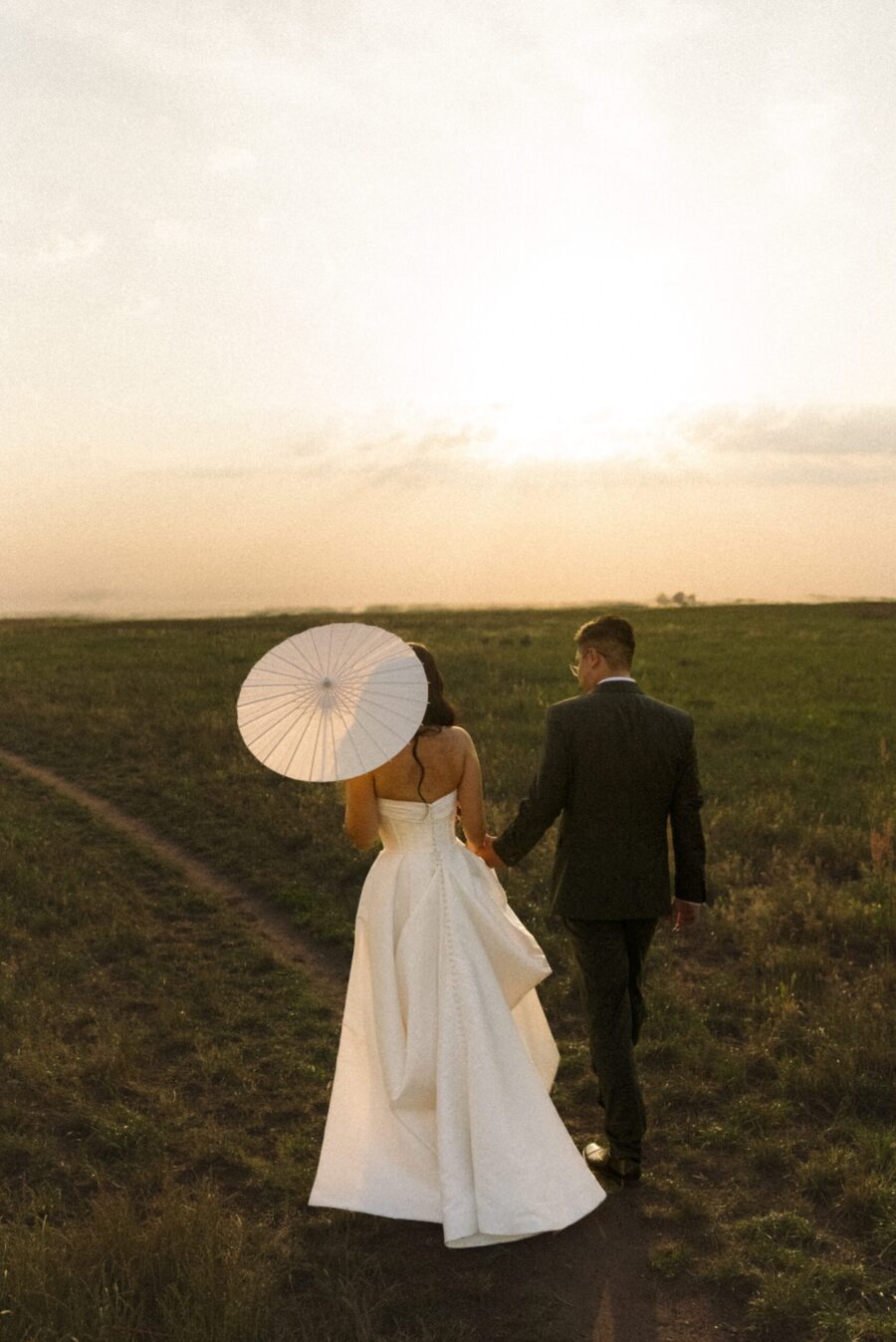 Brautpaar geht mit Sonnenschirm im Feld bei Sonnenuntergang