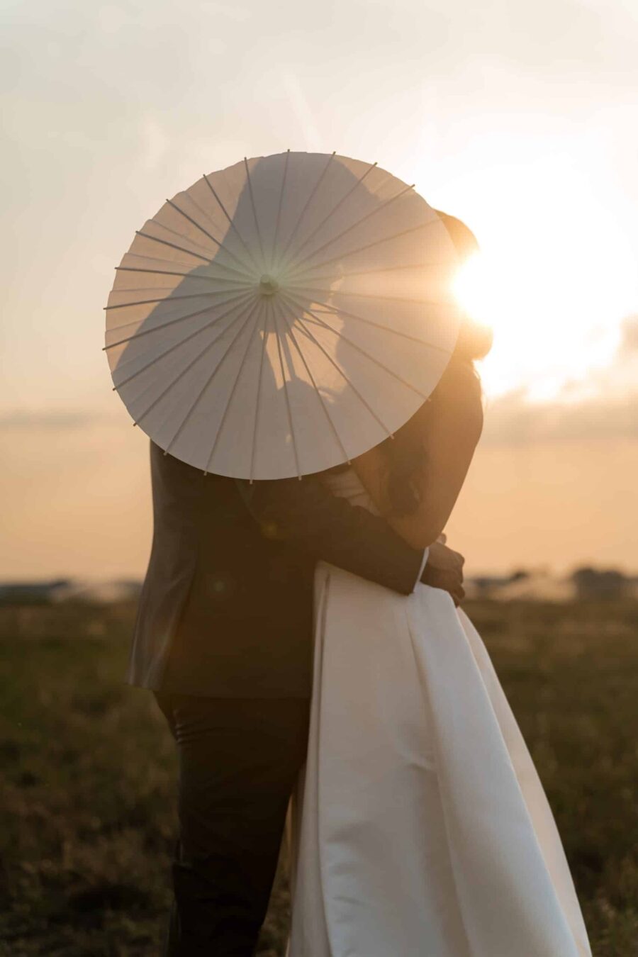Brautpaar hinter Sonnenschirm bei Sonnenuntergang