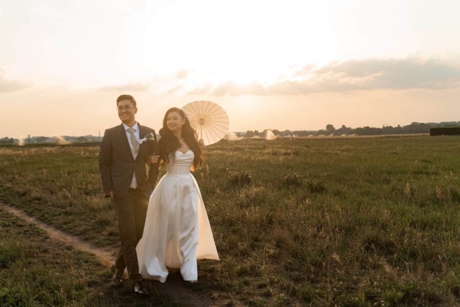 Brautpaar spaziert im Sonnenuntergang auf Feldweg.