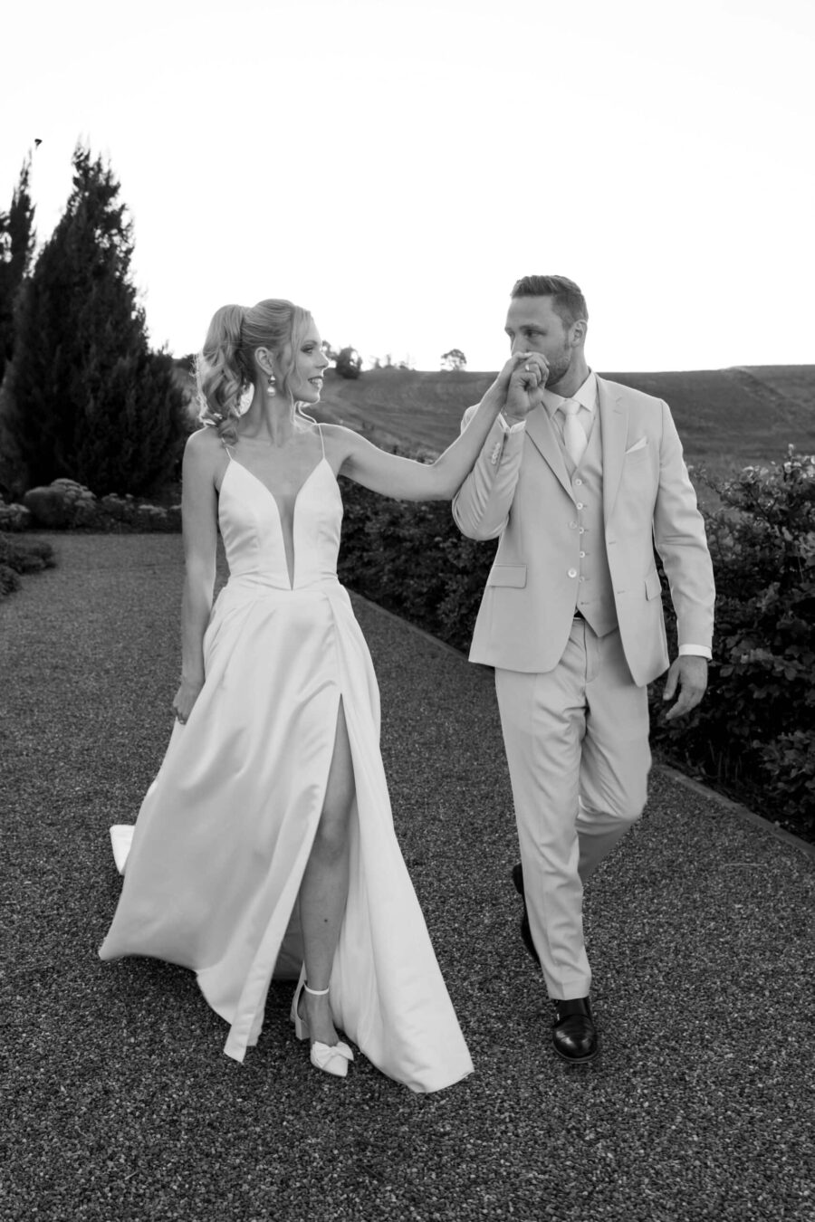 Brautpaar spaziert im Garten in eleganter Hochzeitskleidung.