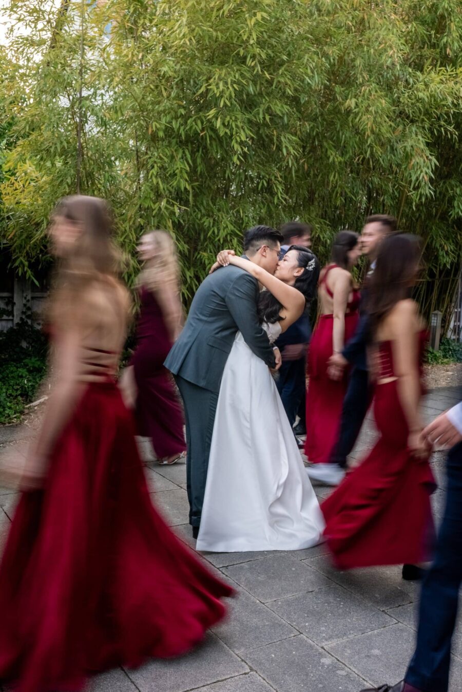 Brautpaar umarmt sich im Garten mit tanzenden Gästen