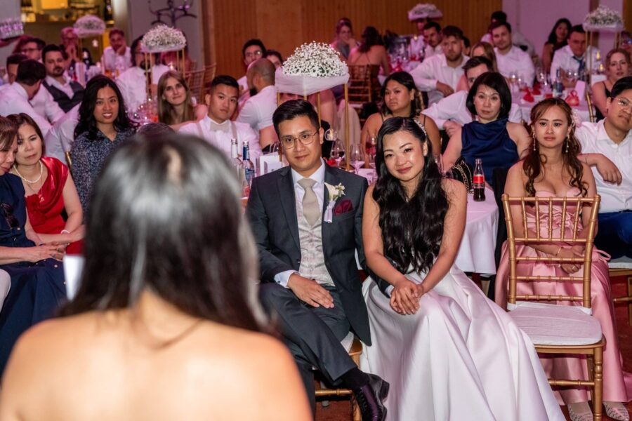 Hochzeitspaar bei Ansprache umgeben von Gästen.