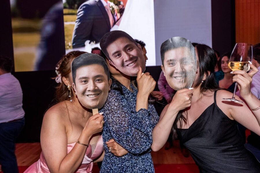 Hochzeitsgäste mit Masken und Weinglas feiern.