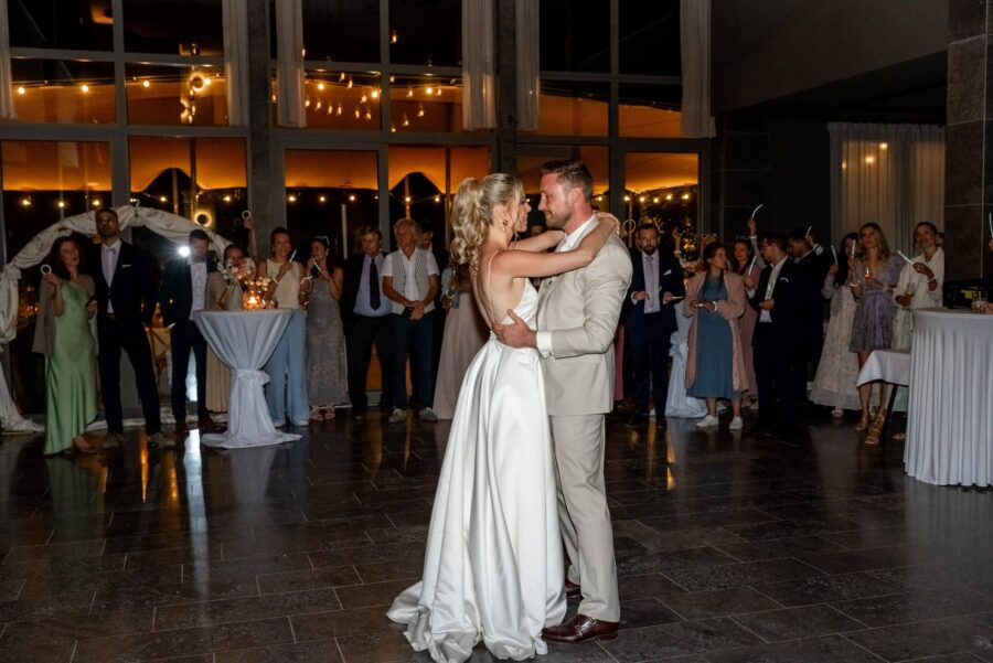 Brautpaar eröffnet Hochzeitstanz, umgeben von Gästen.