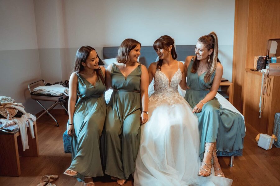 Braut mit Brautjungfern auf Bett im Ankleidezimmer